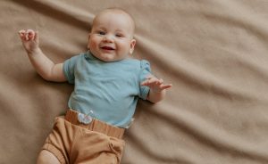 baby in blue shirt and brown shorts lying on brown textile